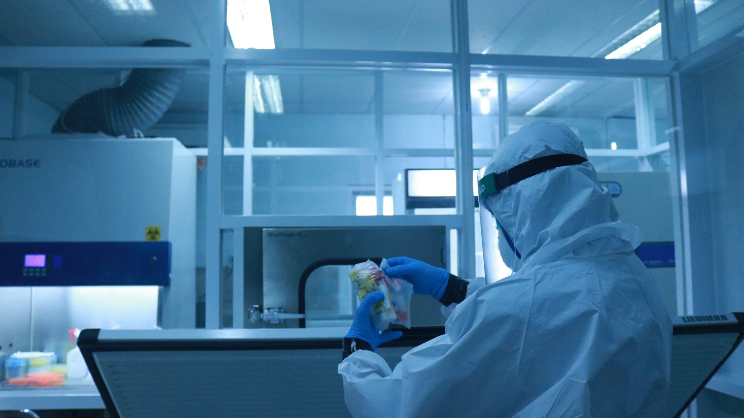 Technician in a full cleanroom suit handling samples at a laboratory workstation